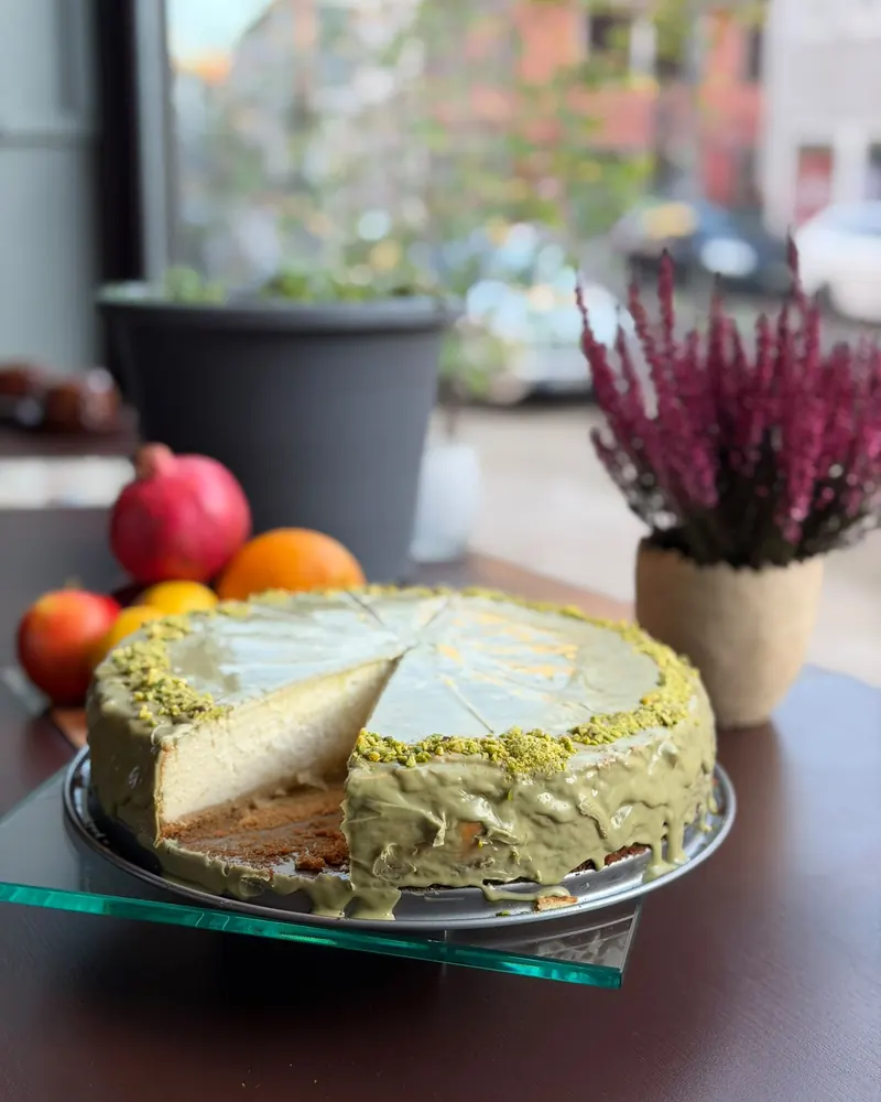 Pistazien-Cheesecake mit grüner Glasur und gehackten Pistazien, angeschnitten auf einer Glasplatte