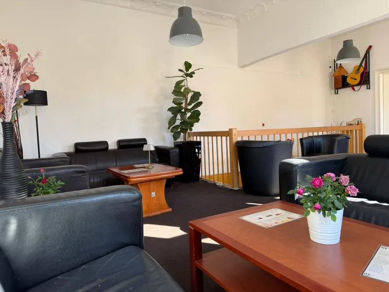 Sitzecke im Chai: Ledersessel, ein Holztisch mit Rosen im Topf, eine große Zimmerpflanze und eine Gitarre an der Wand
